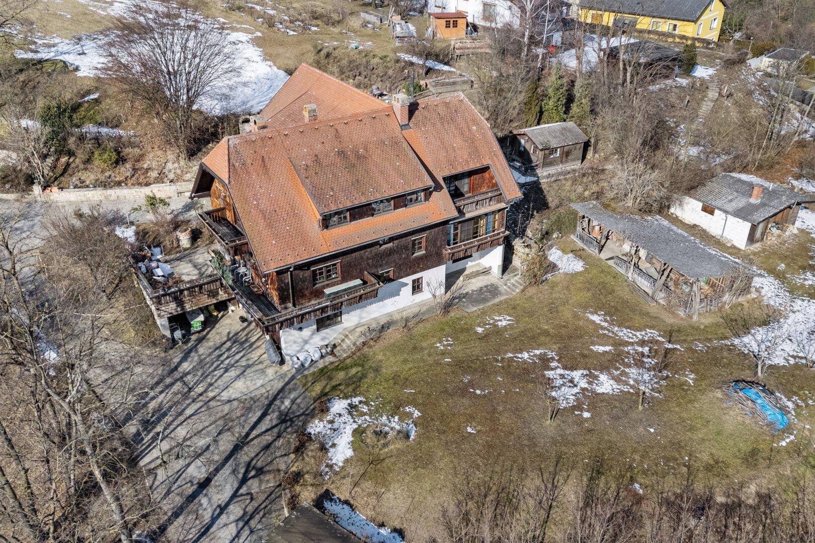 Luftaufnahme des Anwesens mit traditionellem Haus und umliegender, teilweise schneebedeckter Landschaft.