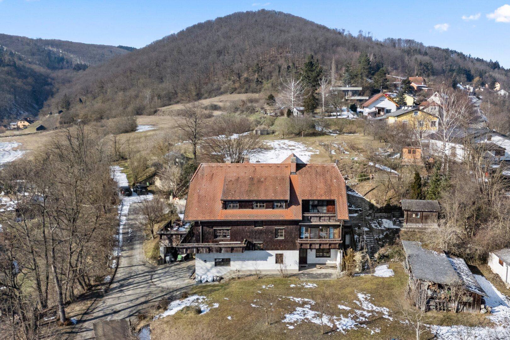 Weitläufige Luftaufnahme des Anwesens mit Haus und umliegender Hügellandschaft im Winter.