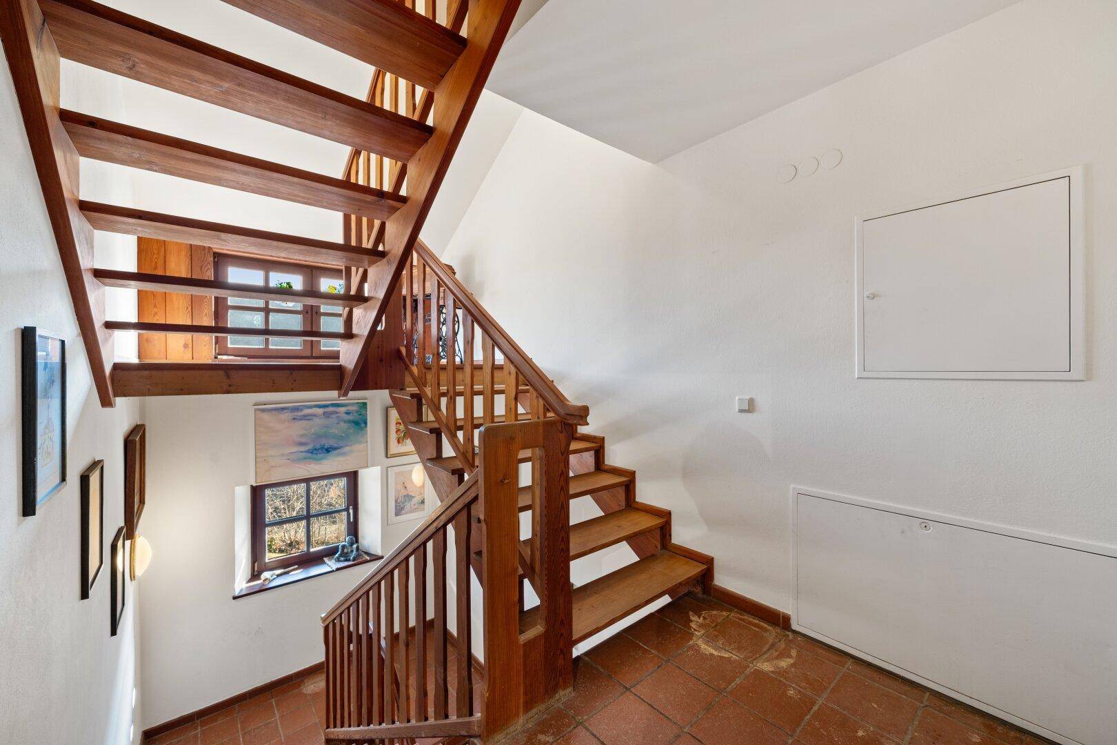 Helles Treppenhaus mit Holztreppe und Terrakottafliesen, das die verschiedenen Ebenen verbindet.