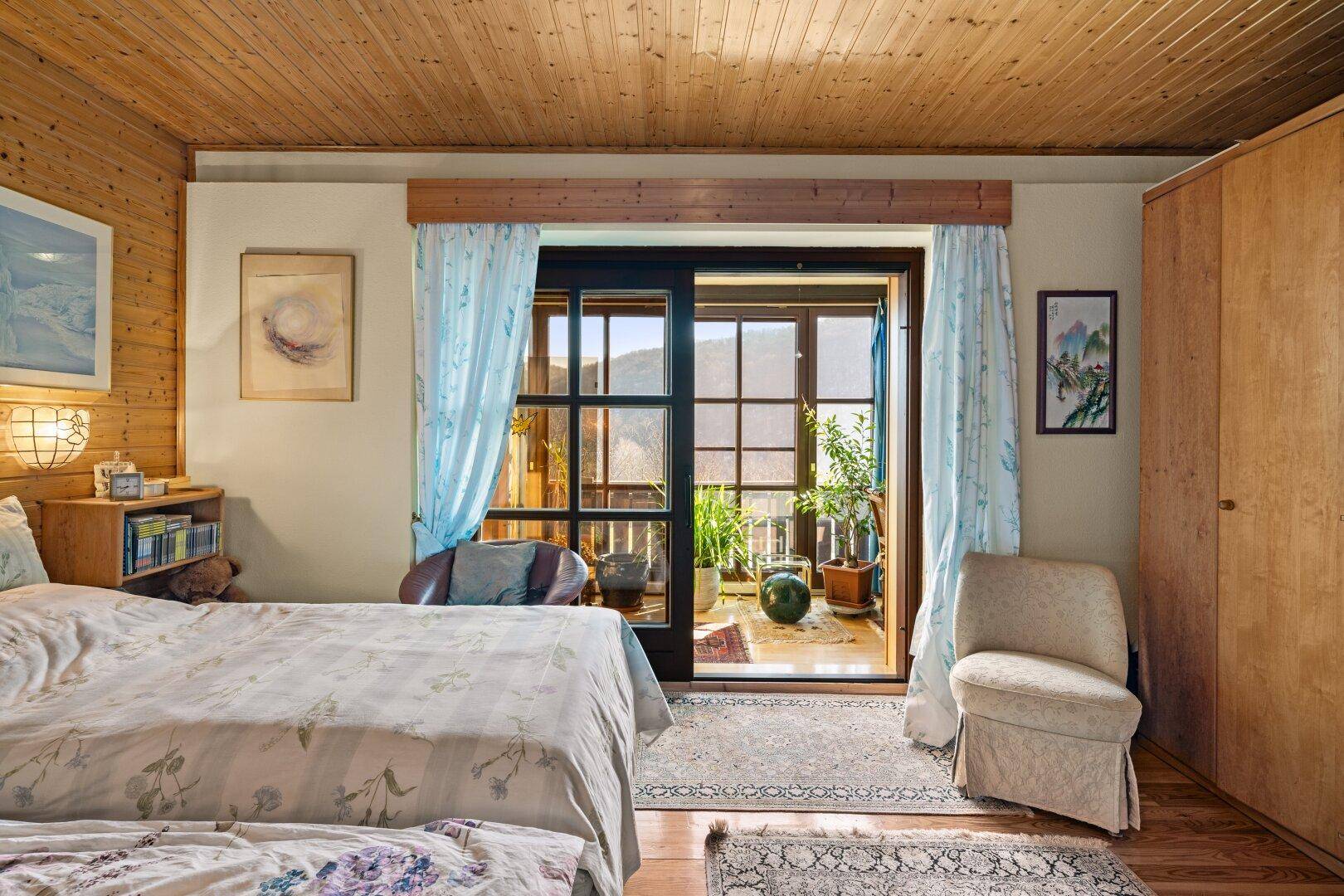 Gemütliches Schlafzimmer mit Holzdecke, Doppelbett und direktem Zugang zum Balkon.