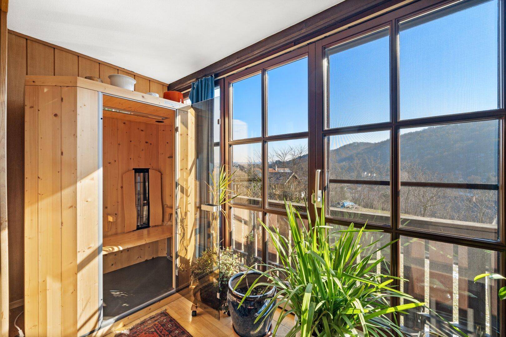 Heller Wintergarten mit integrierter Sauna und weitem Blick auf die umliegende Landschaft.