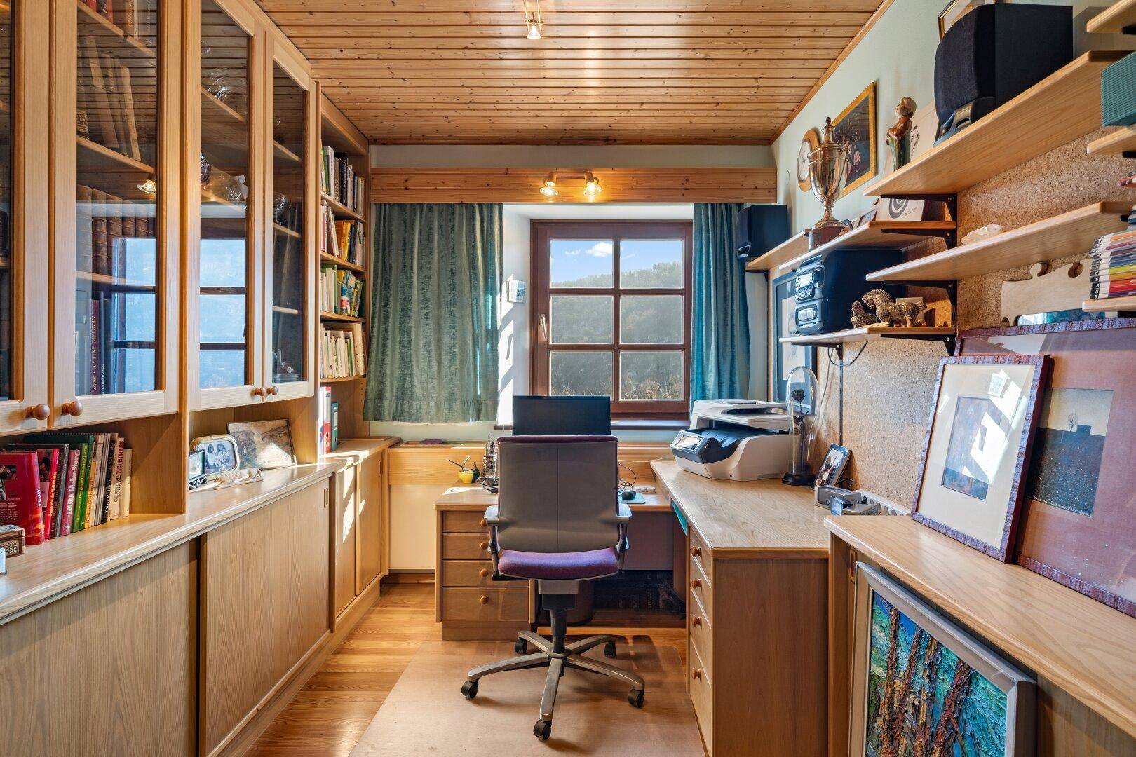 Funktionales Büro mit Holzmöbeln, Regalen und Blick ins Grüne.