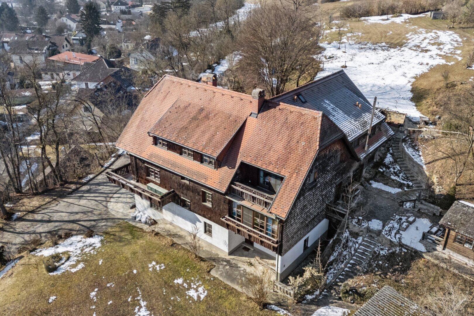 Luftaufnahme des Anwesens mit traditionellem Haus und umliegender, teilweise schneebedeckter Landschaft.