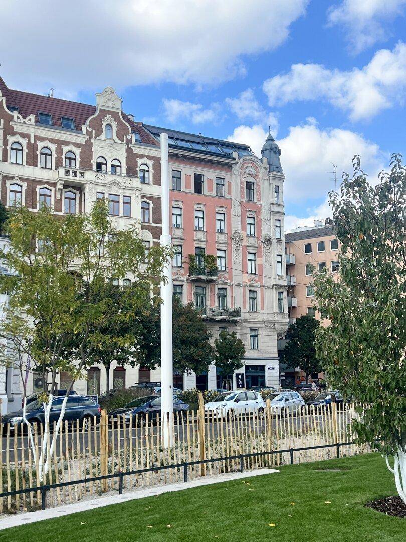 Historische Gebäude mit klassischer Architektur entlang einer begrünten Straße unter blauem Himmel.