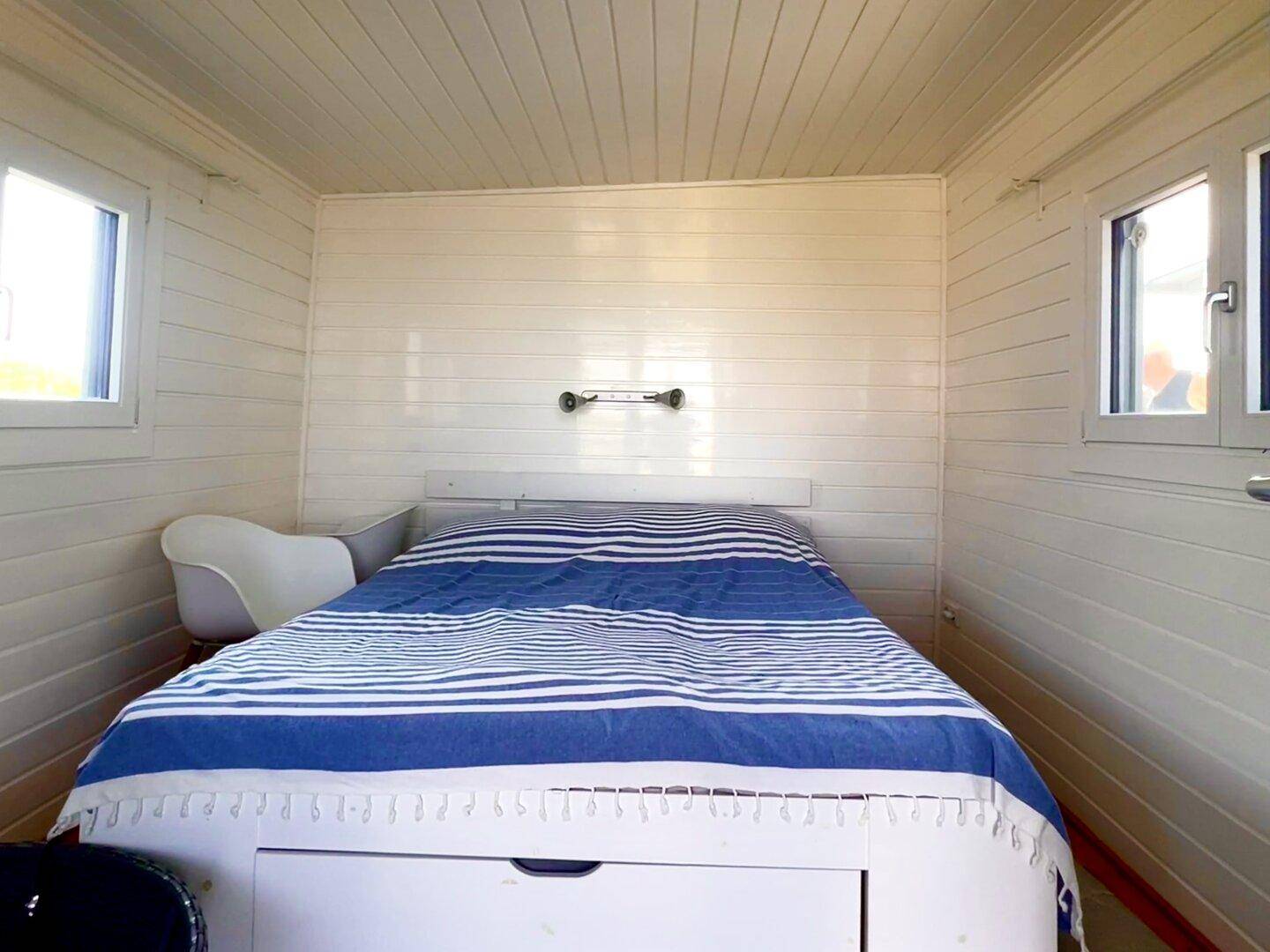 Helles Schlafzimmer mit weiß getäfelten Wänden, Holzboden und zwei Fenstern für viel Tageslicht.