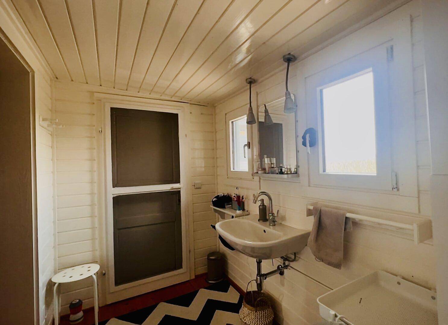 Badezimmer mit Waschbecken, Fenster und Zugang zu einem weiteren Bereich, hell und funktional.