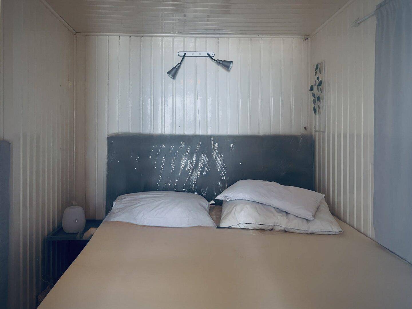 Einfaches Schlafzimmer mit Doppelbett, weiß getäfelten Wänden und Leselampen für gemütliche Abende.