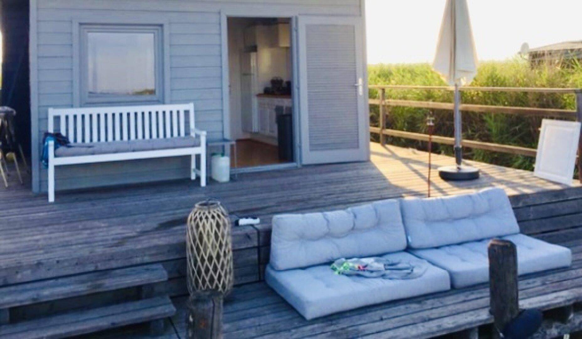 Gemütliche Holzterrasse mit Sitzgelegenheiten und Blick auf das Wasser und die Natur am sonnigen Tag.
