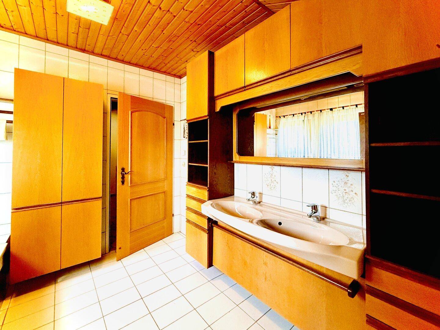 Badezimmer mit Doppelwaschbecken, Holzdecke und hellen Fliesen.