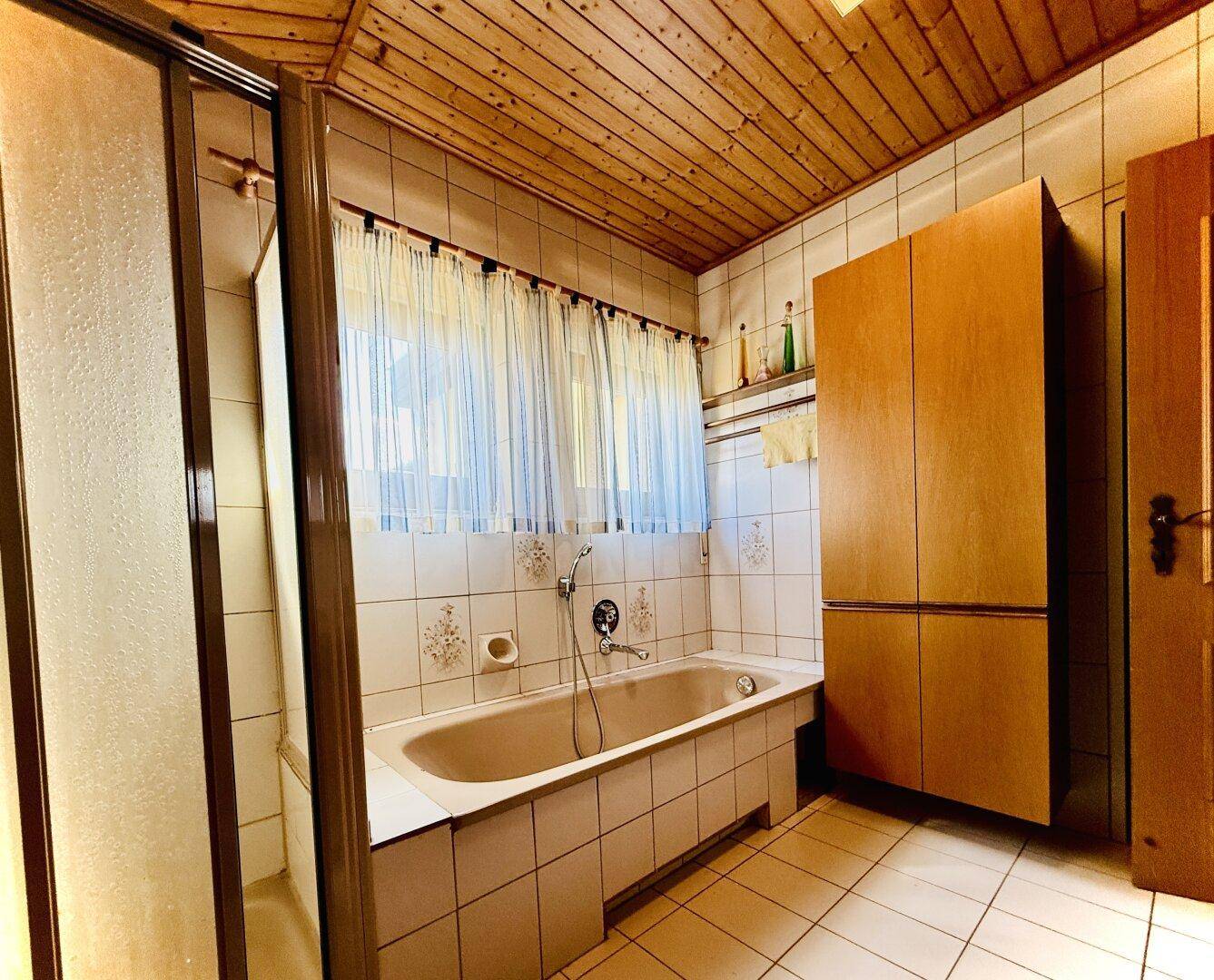 Badezimmer mit Badewanne, Duschkabine und Holzdecke, hell gefliest.
