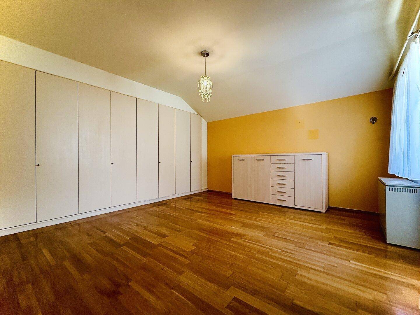 Helles Schlafzimmer mit Parkettboden und einer langen Reihe Einbauschränken.