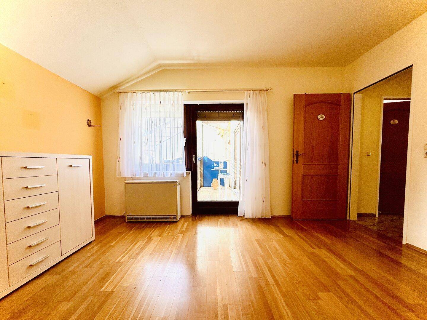 Schlafzimmer mit Parkettboden und direktem Zugang zu einem verglasten Balkon.