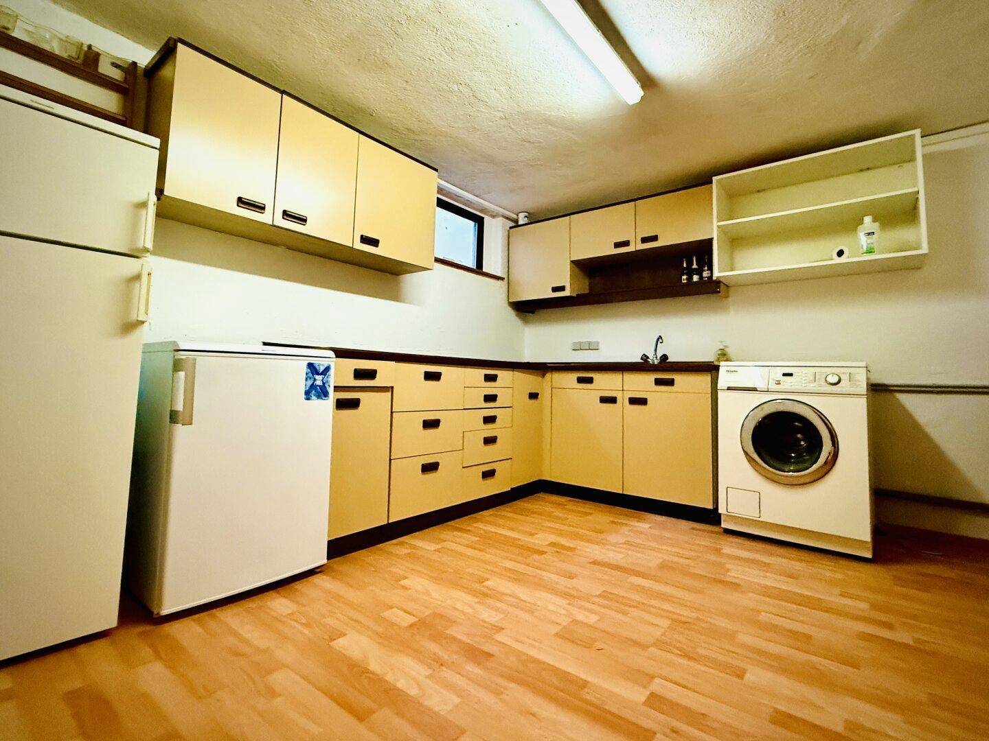 Praktischer Hauswirtschaftsraum im Keller mit Waschmaschine, Kühlschrank und Schränken.