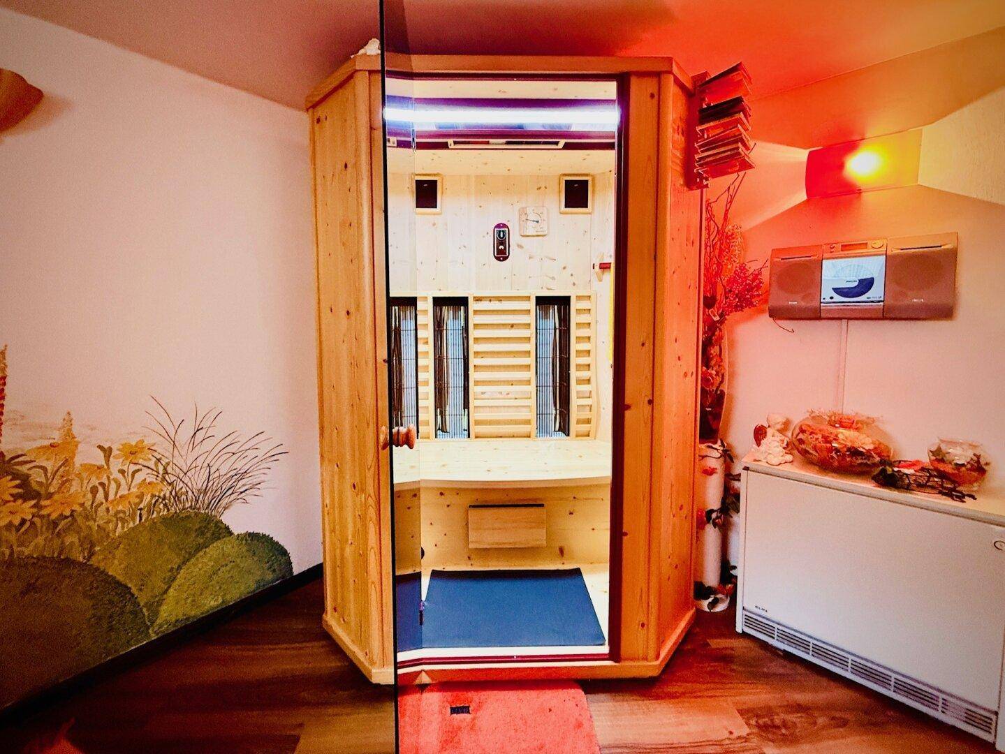 Gemütliche Holzsauna mit Glastür und Infrarotlicht, integriert in einen Raum mit dekorativer Wandmalerei.