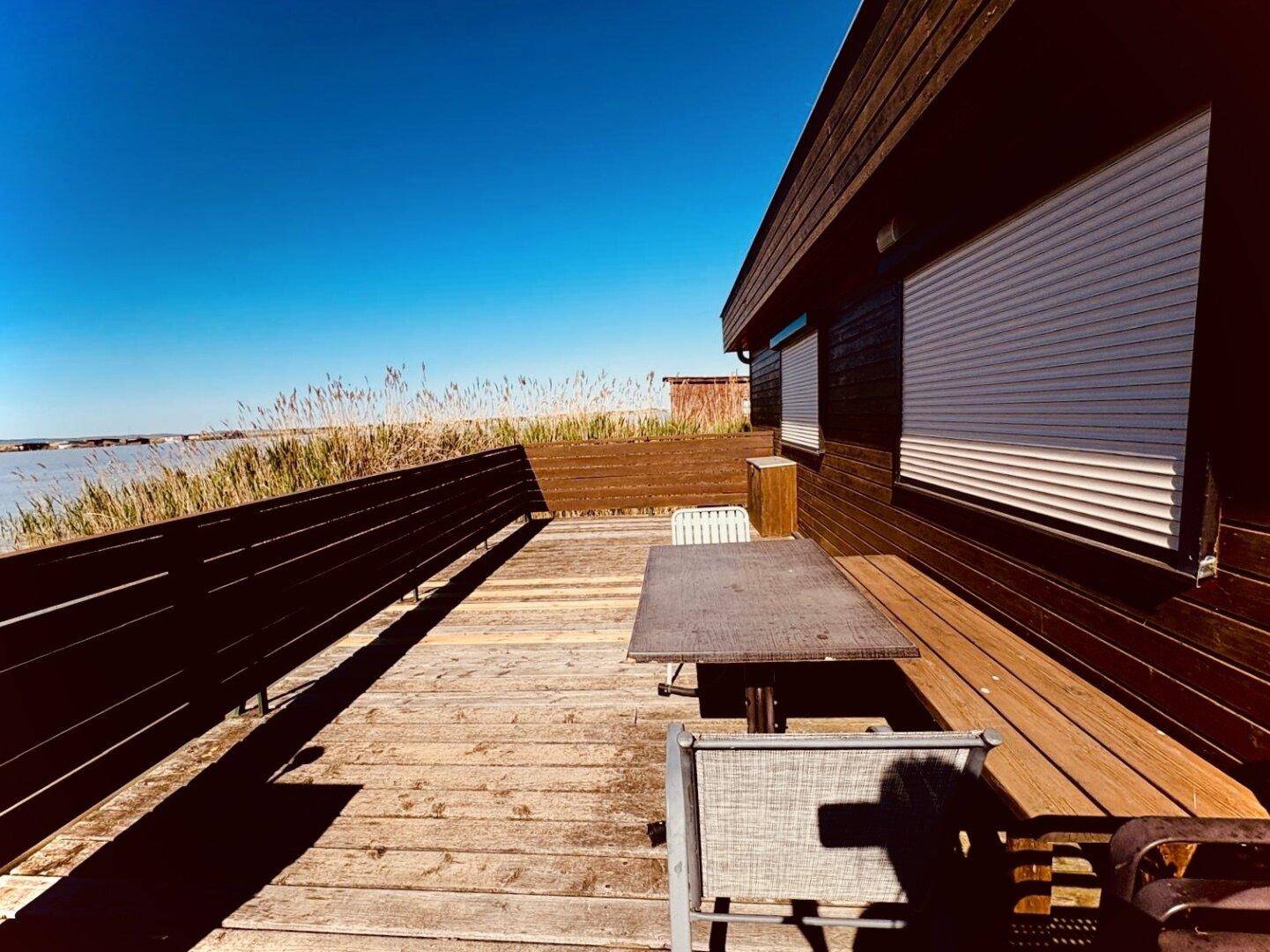 Geräumige Holzterrasse mit Outdoor-Möbeln und weitem Blick auf den See und das Schilf.