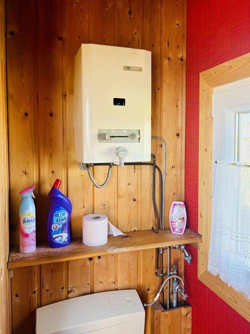 Detailansicht eines Warmwasserbereiters über der Toilette in einem Badezimmer mit roter Wand.