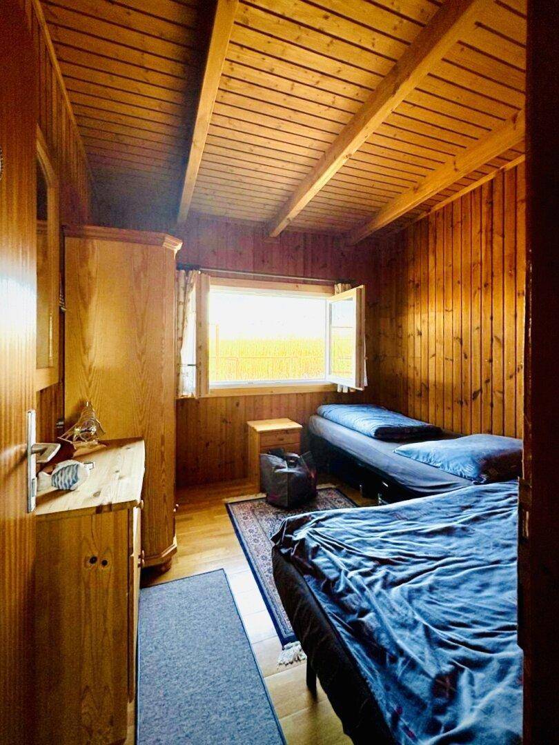Helles Schlafzimmer mit zwei Einzelbetten, Holzverkleidung und Blick auf die Landschaft.