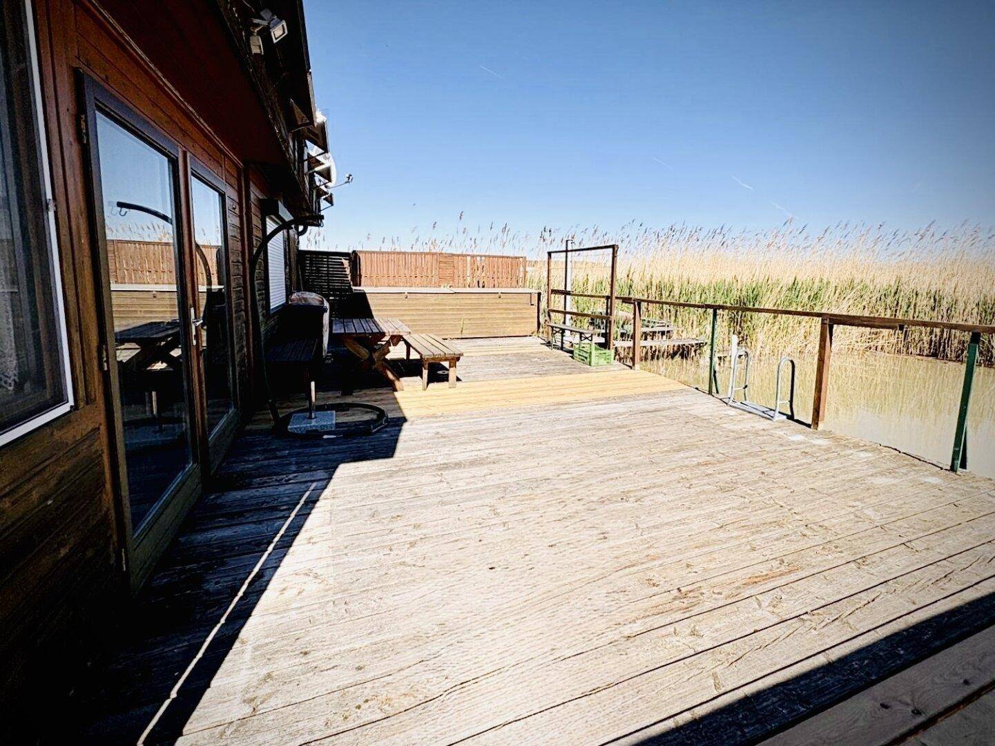 Weitläufige Holzterrasse neben dem Haus mit Blick auf das Wasser und die umliegende Natur.