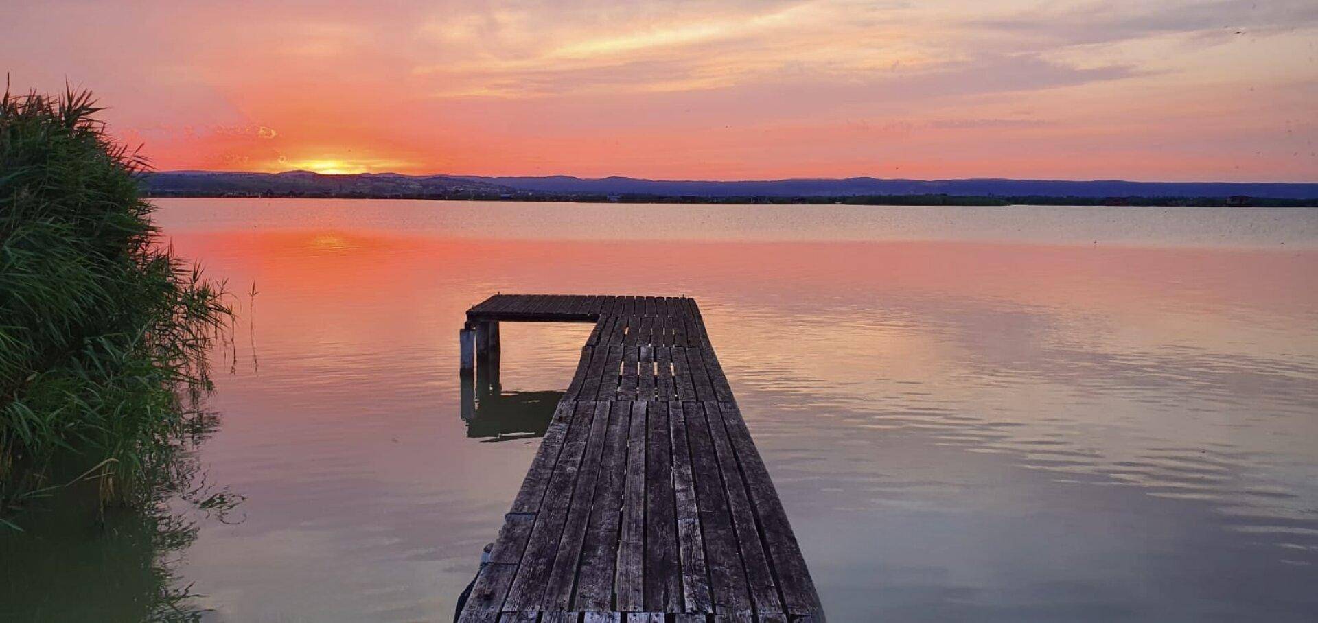 Atemberaubender Sonnenuntergang über dem See, mit einem langen Holzsteg, der ins ruhige Wasser ragt.