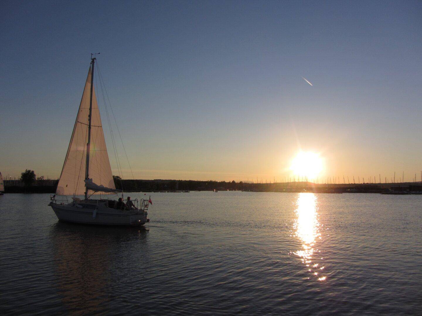 Segelboot auf dem Wasser bei Sonnenuntergang mit malerischem Blick über den See.