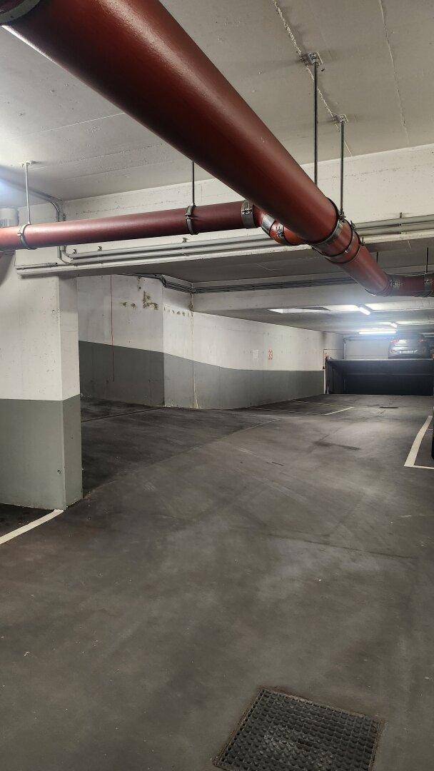 Geräumige Tiefgarage mit Betonboden, klaren Markierungen und sichtbaren Rohren an der Decke.