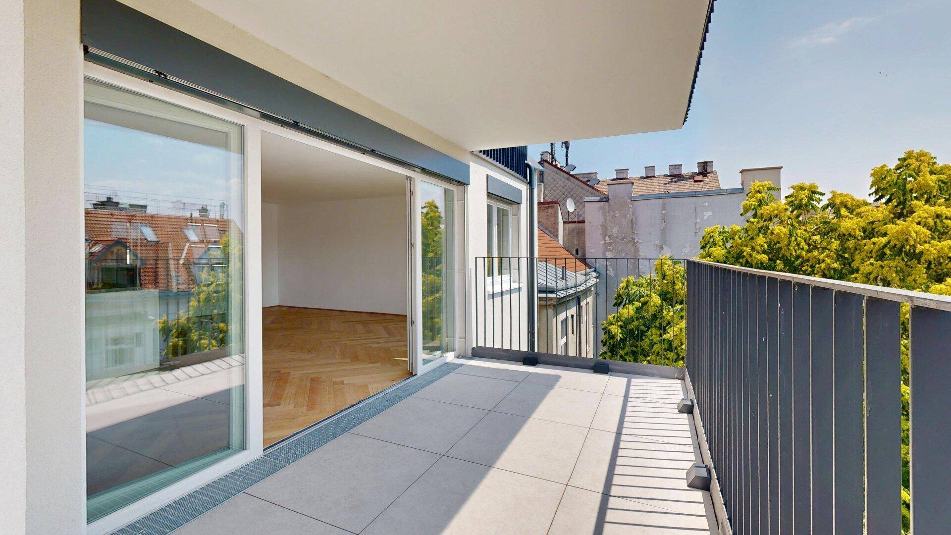 Sonniger Balkon mit Fliesenboden und Blick auf die Stadt und Bäume, einladend und offen.