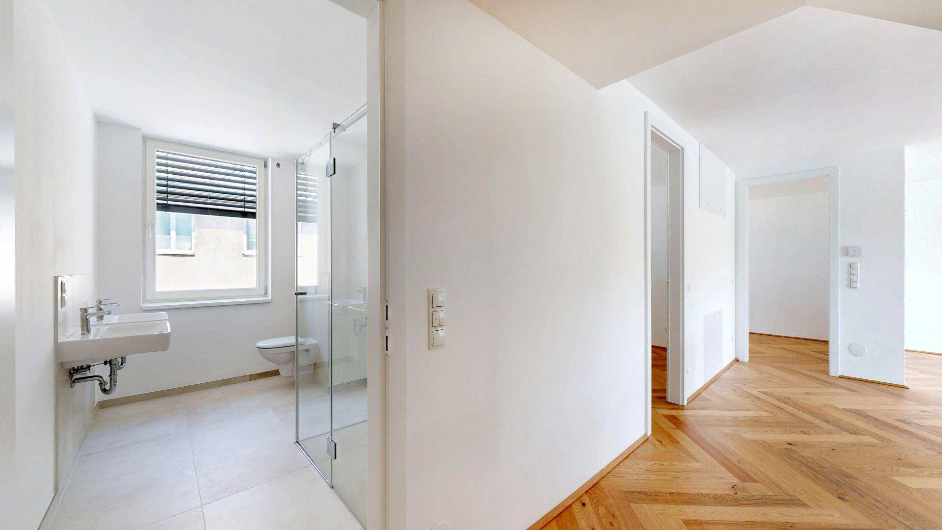 Modernes Badezimmer mit Dusche, Waschbecken und Fenster, helle Fliesen und minimalistisches Design.