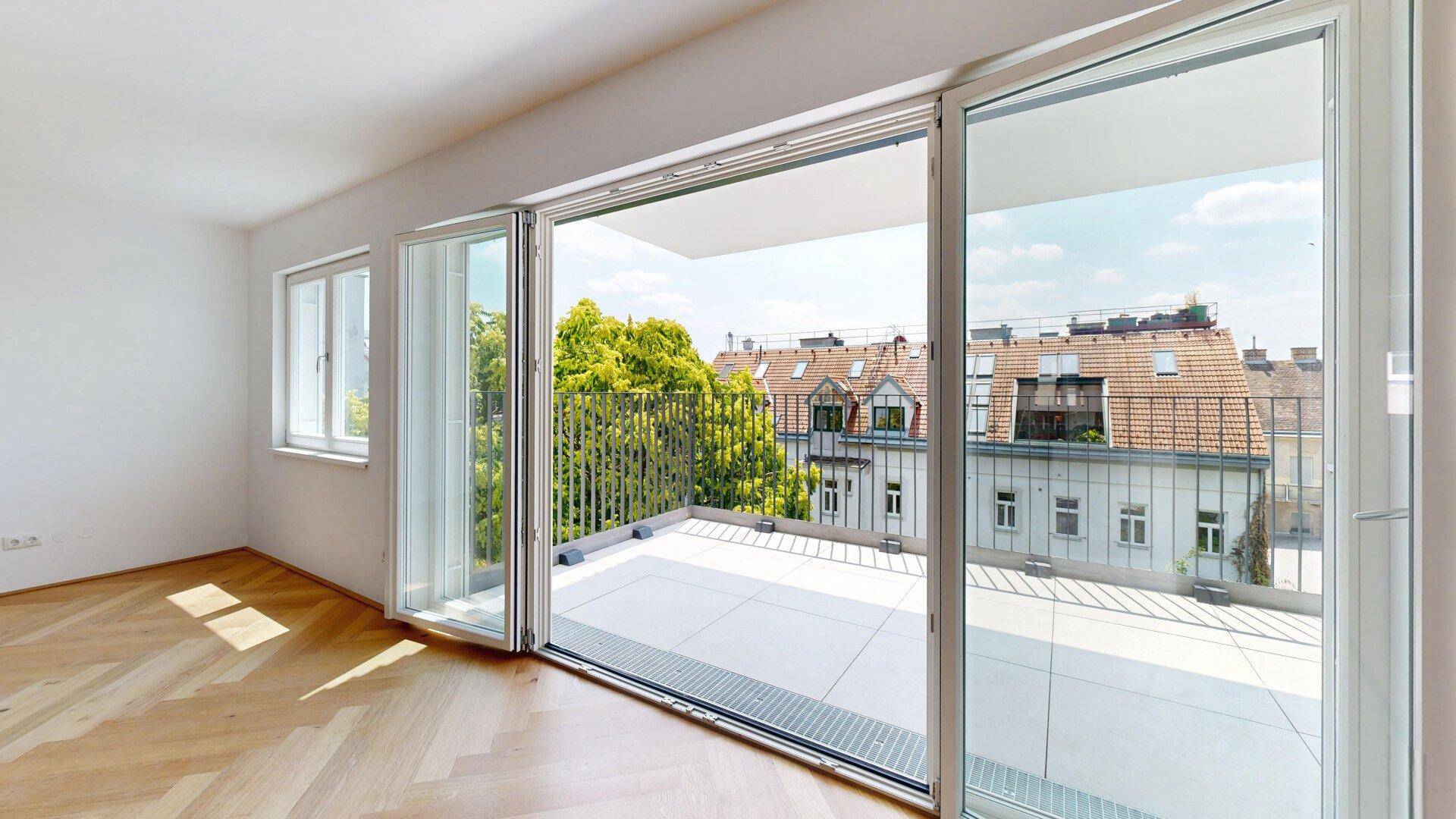 Helles Wohnzimmer mit Fischgrätparkett und großzügigem Zugang zum Balkon, viel Tageslicht.