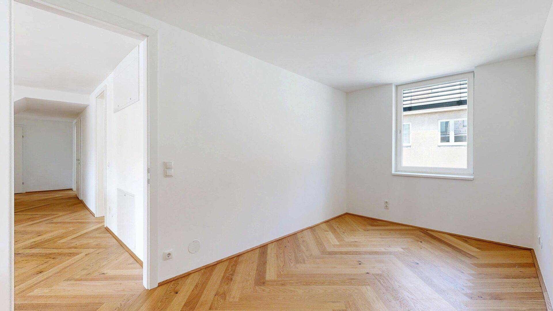 Geräumiges Zimmer mit Fischgrätparkett und Fenster, viel Platz für individuelle Gestaltung.