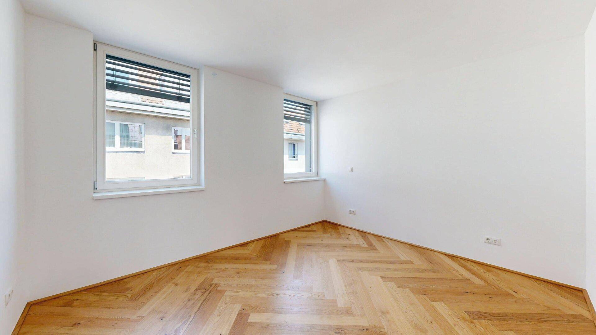 Geräumiges Zimmer mit Fischgrätparkett und zwei Fenstern, ideal als Schlaf- oder Arbeitszimmer.