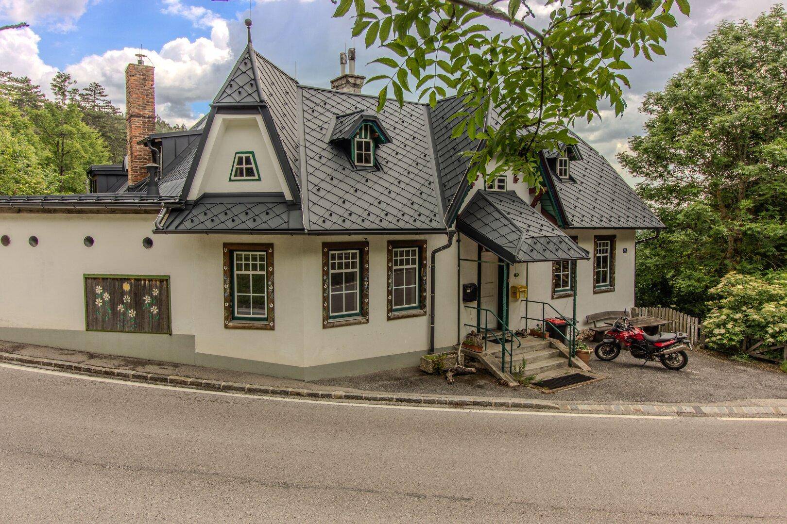 Charmantes Haus mit Mansarddach, weißen Fassaden und grünen Fensterrahmen an einer Straße.