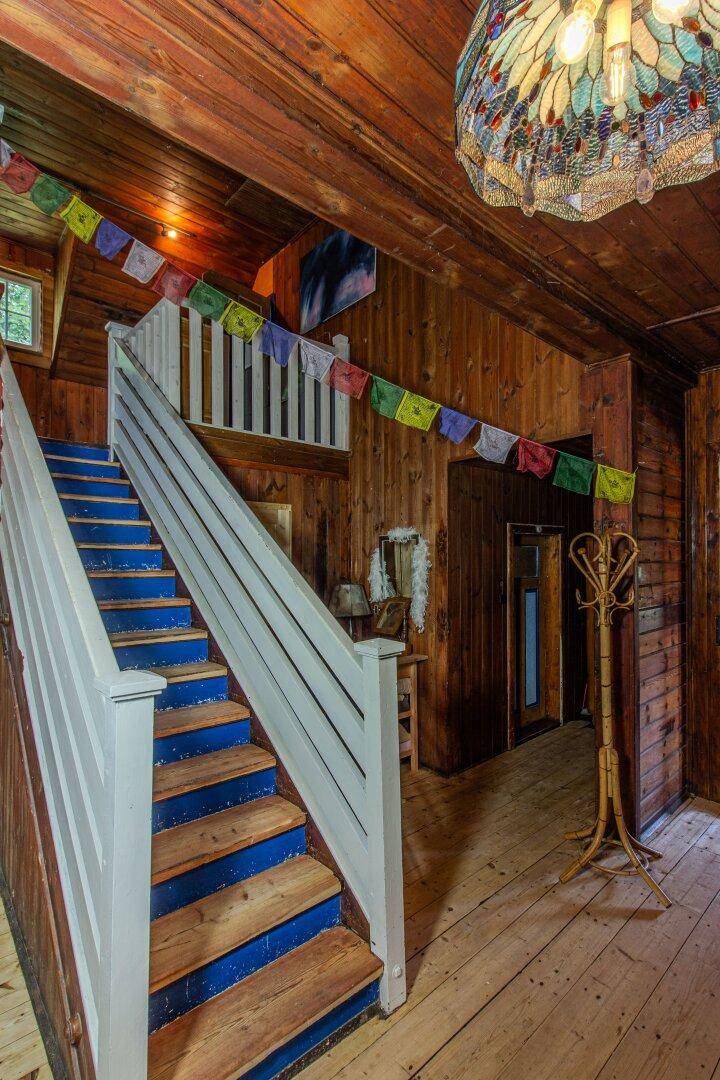 Treppenhaus mit Holzvertäfelung, bunten Gebetsfahnen und einem dekorativen Kronleuchter.