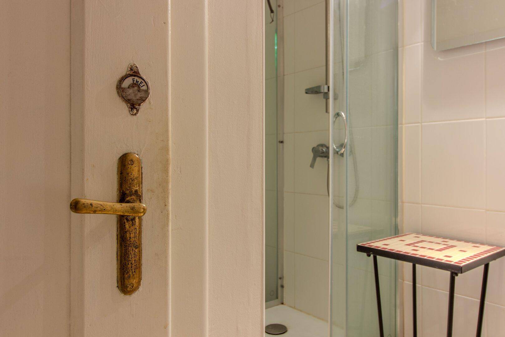 Badezimmer mit einfacher Duschkabine und einer Tür mit rustikalem Griff.