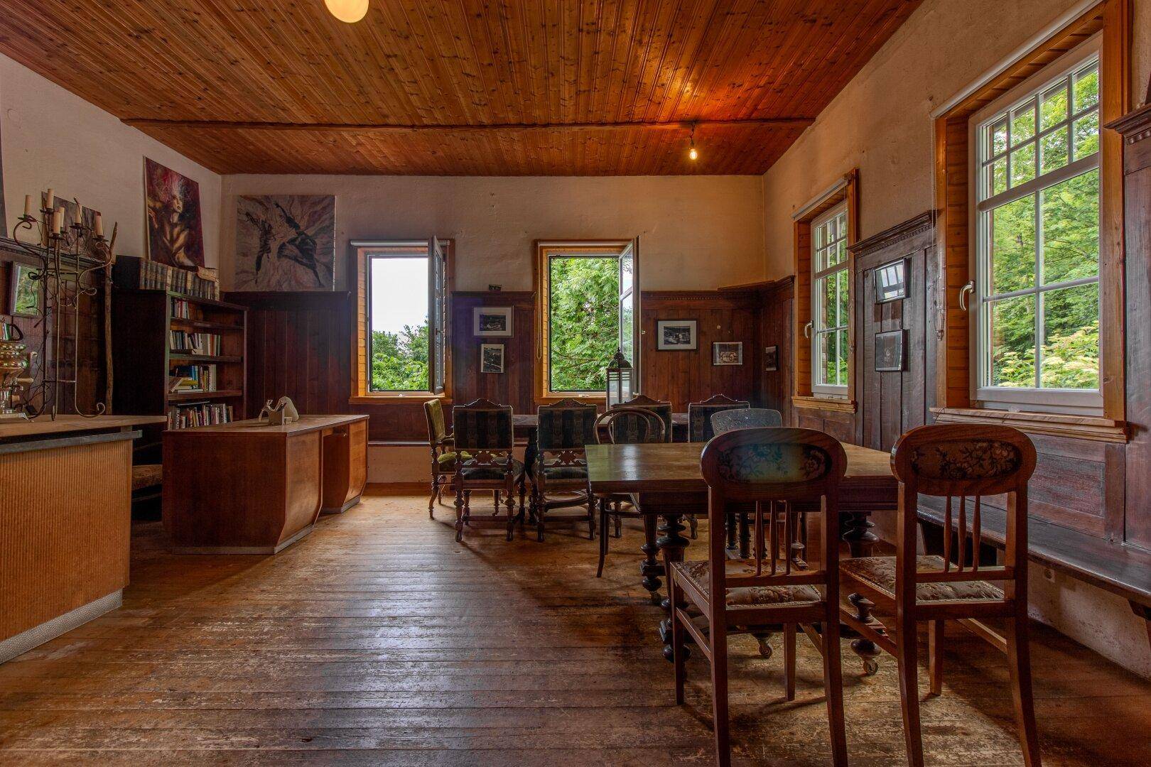 Arbeitszimmer mit Holzboden, Bücherregalen und Fenstern, die viel Tageslicht hereinlassen.