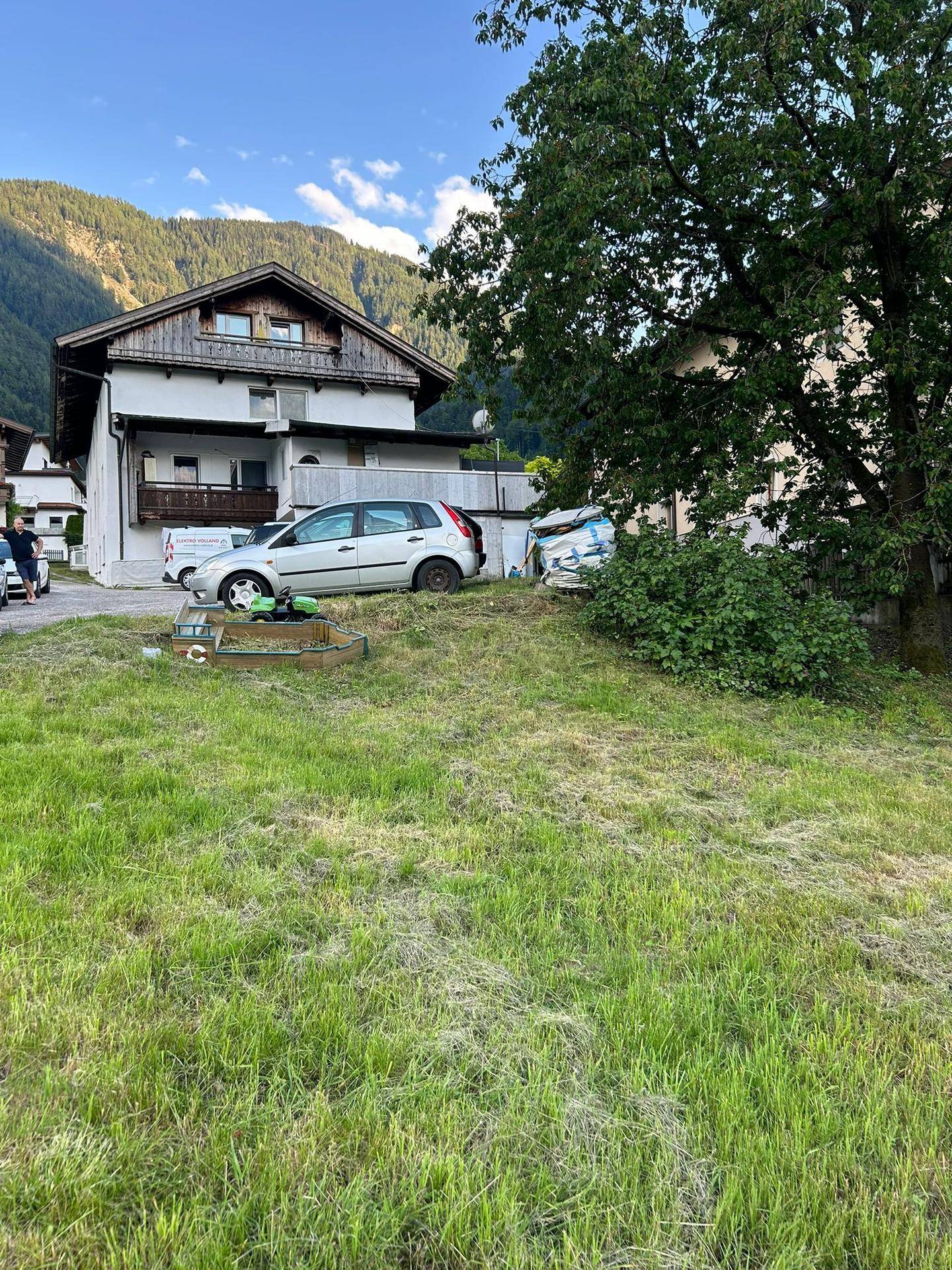 Mehrfamilienhaus in ländlicher Umgebung mit Bergblick und gepflegter Grünfläche im Vordergrund.