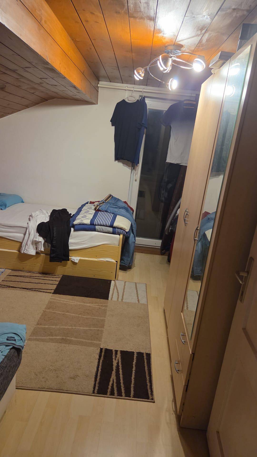 Gemütliches Schlafzimmer mit Holzbalkendecke, Dachschräge und großem Kleiderschrank mit Spiegeltür.