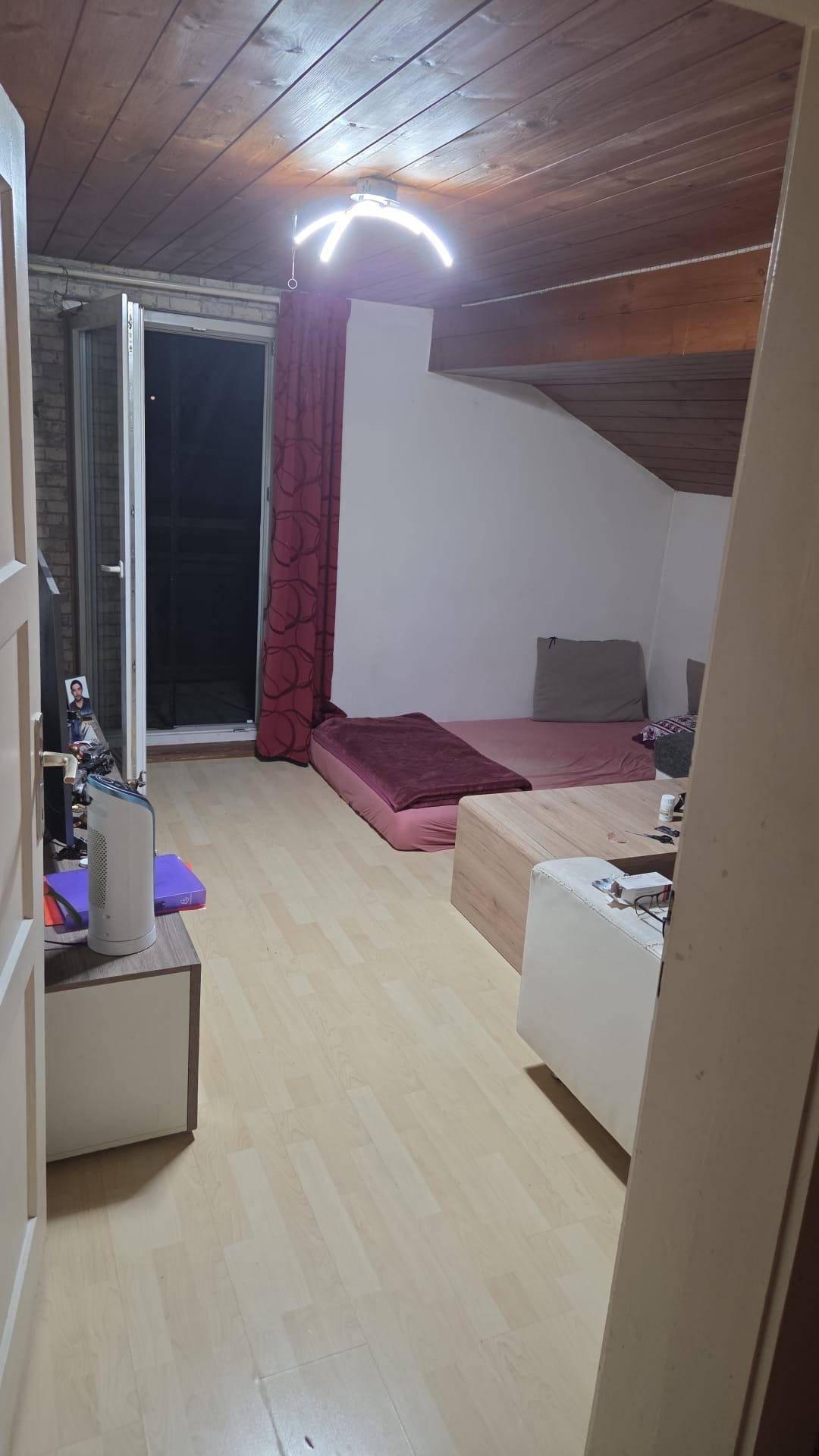 Schlafzimmer im Dachgeschoss mit Holzbalkendecke, Dachschräge und Zugang zu einem Balkon.