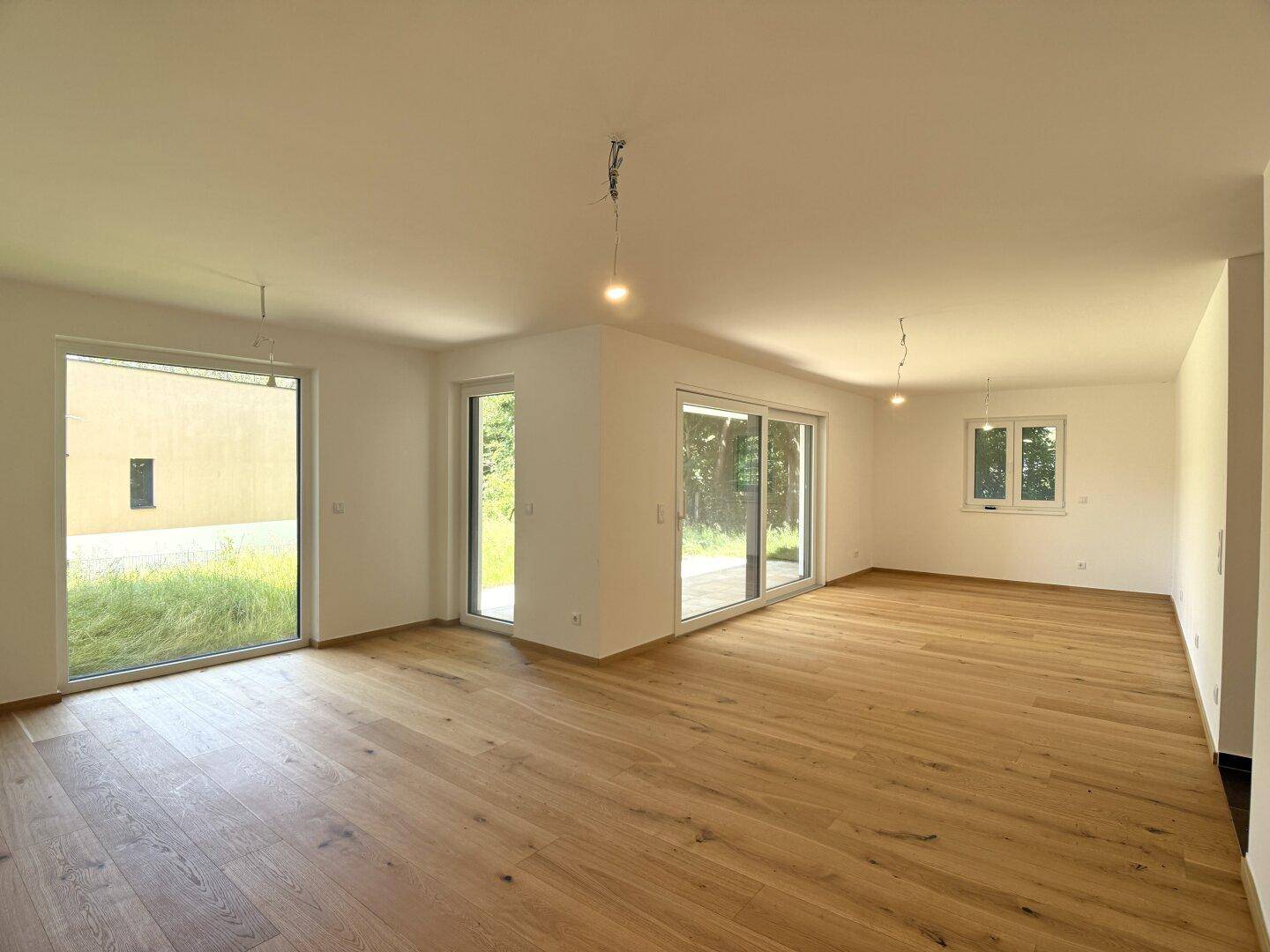 Heller, leerer Wohnraum mit modernem Holzparkett und großen Schiebetüren zur Terrasse.