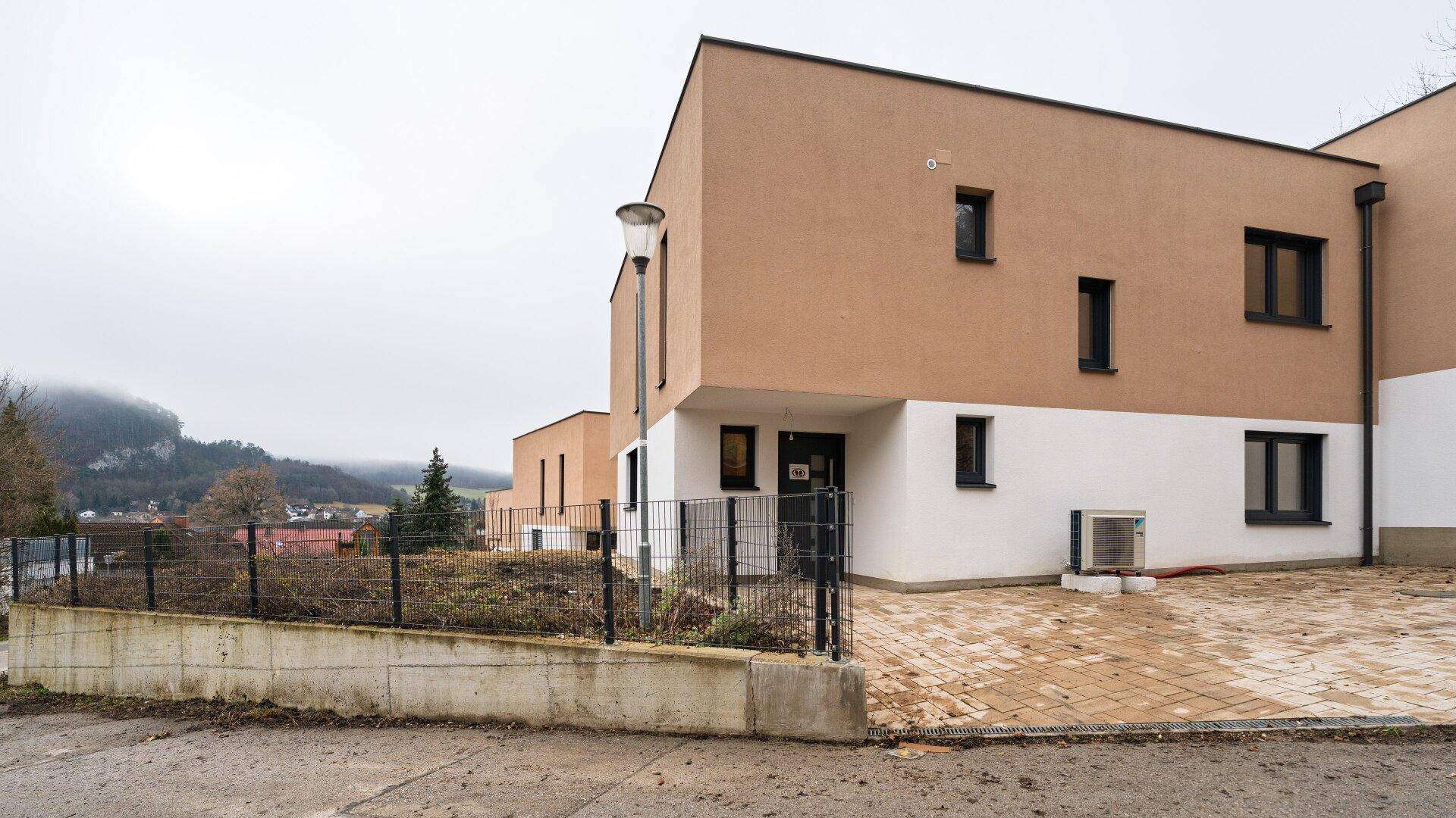 Moderne Architektur des Hauses mit gepflastertem Eingangsbereich und Blick auf die umliegende Landschaft.