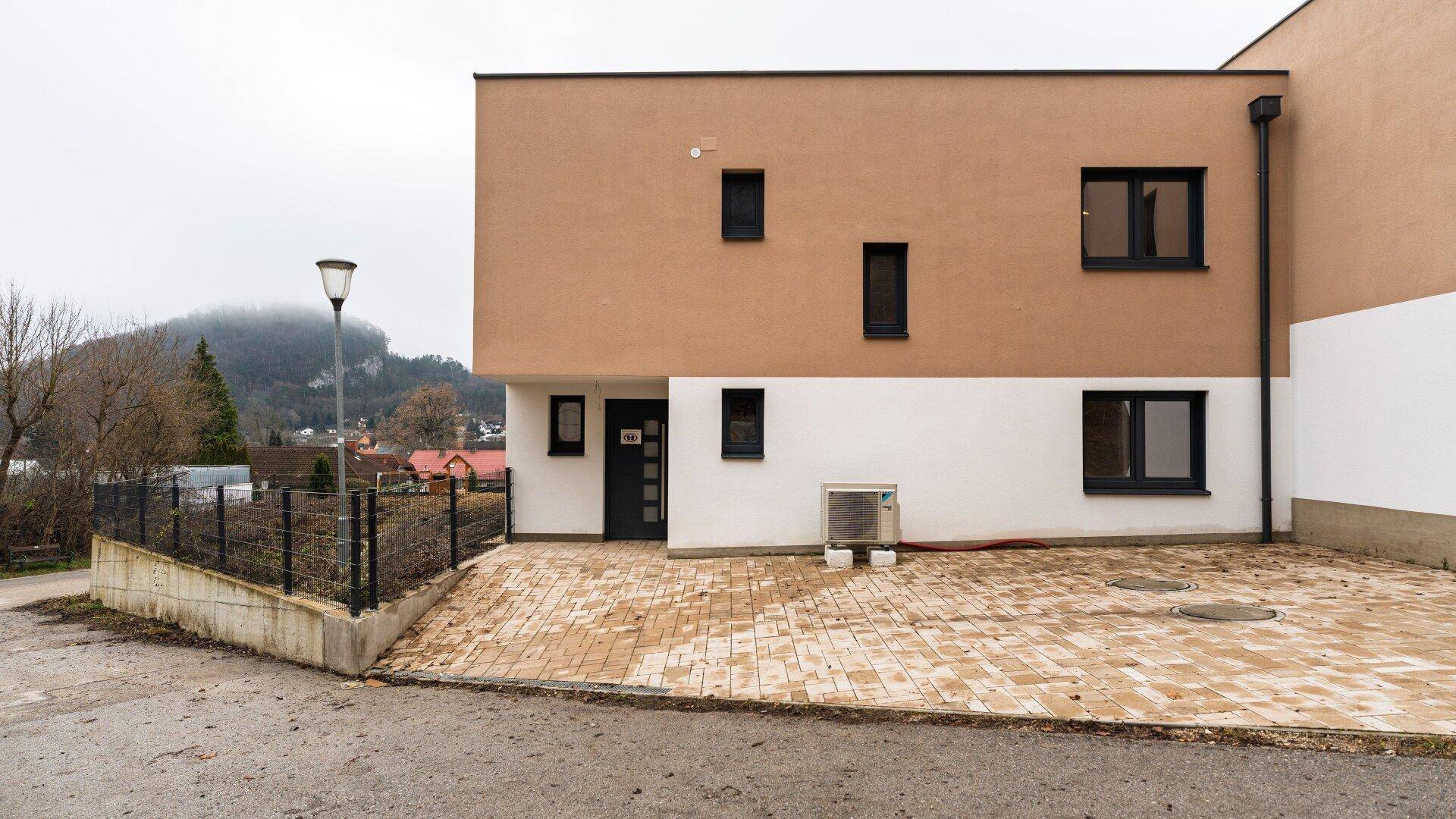 Vorderansicht des modernen Gebäudes mit Eingangsbereich und gepflasterter Zufahrt.