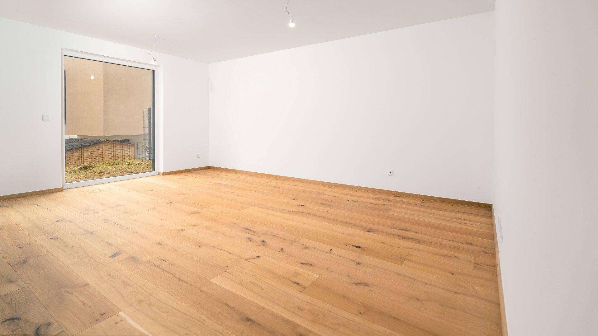 Lichtdurchfluteter Raum mit Holzboden und einer großen Glastür, die den Blick nach draußen freigibt.