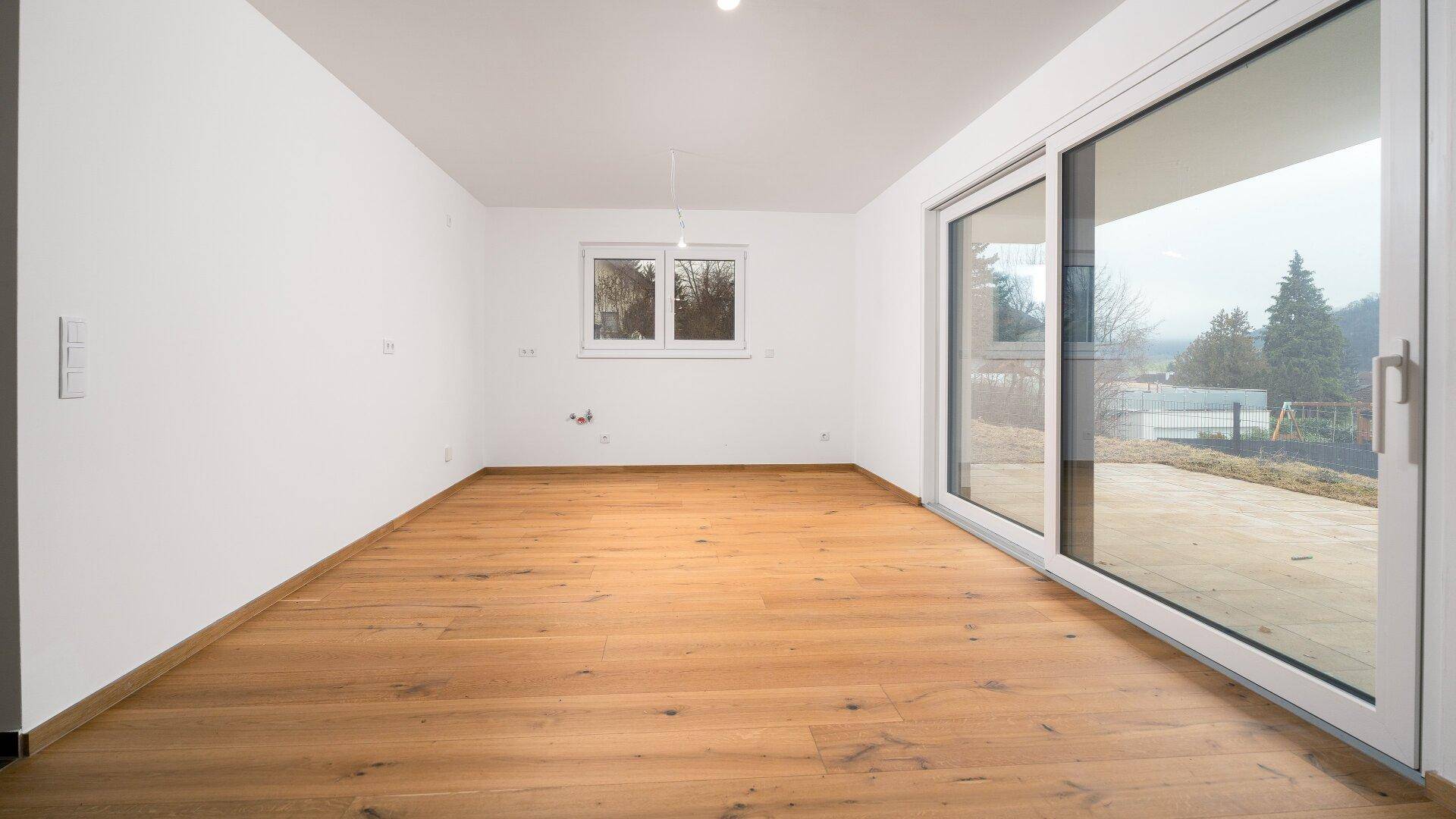 Geräumiger, heller Wohnbereich mit Holzboden und Zugang zur Terrasse durch eine große Schiebetür.