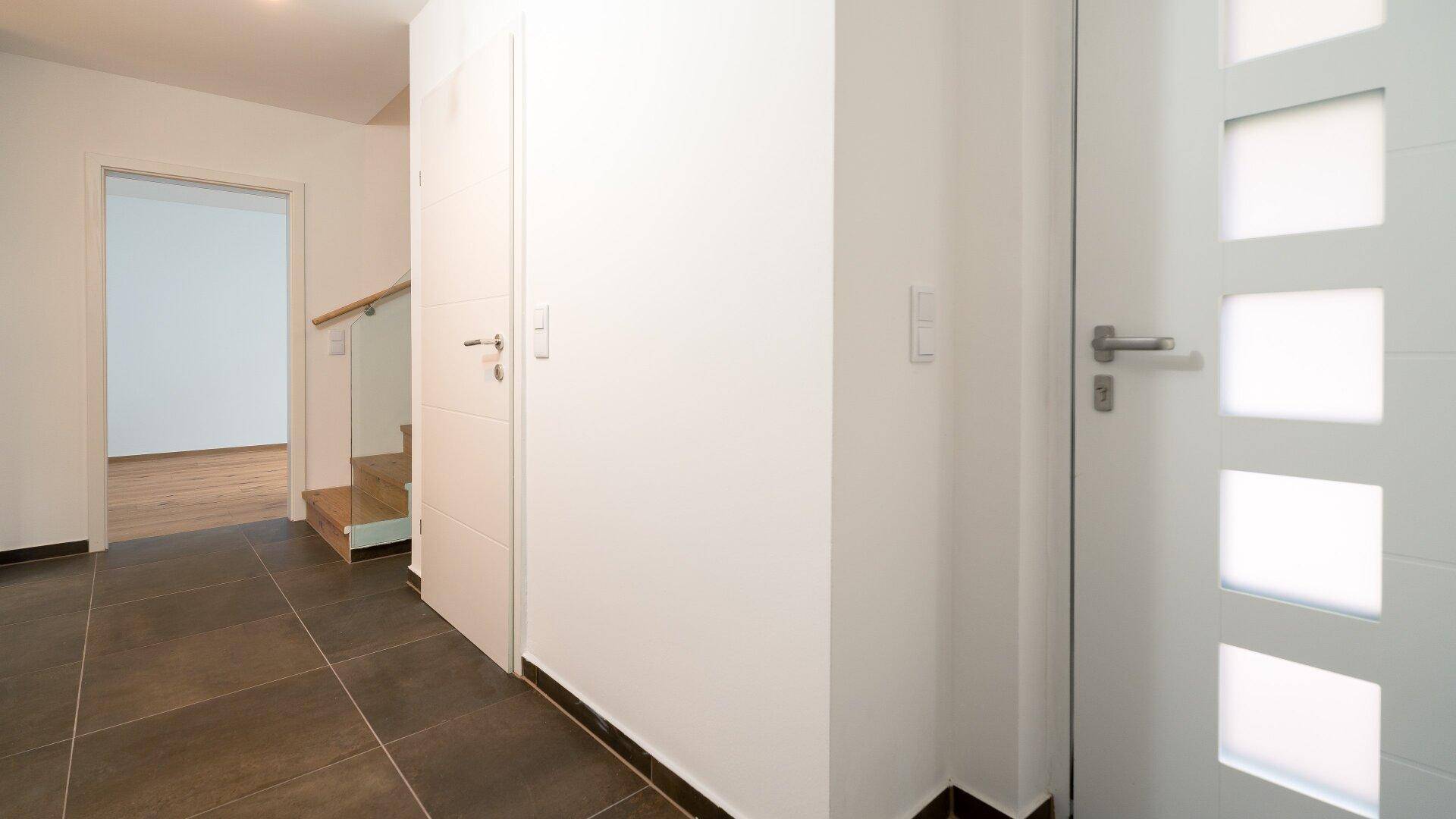 Heller Eingangsbereich mit dunklen Fliesen und moderner weißer Tür, führt zur Treppe.