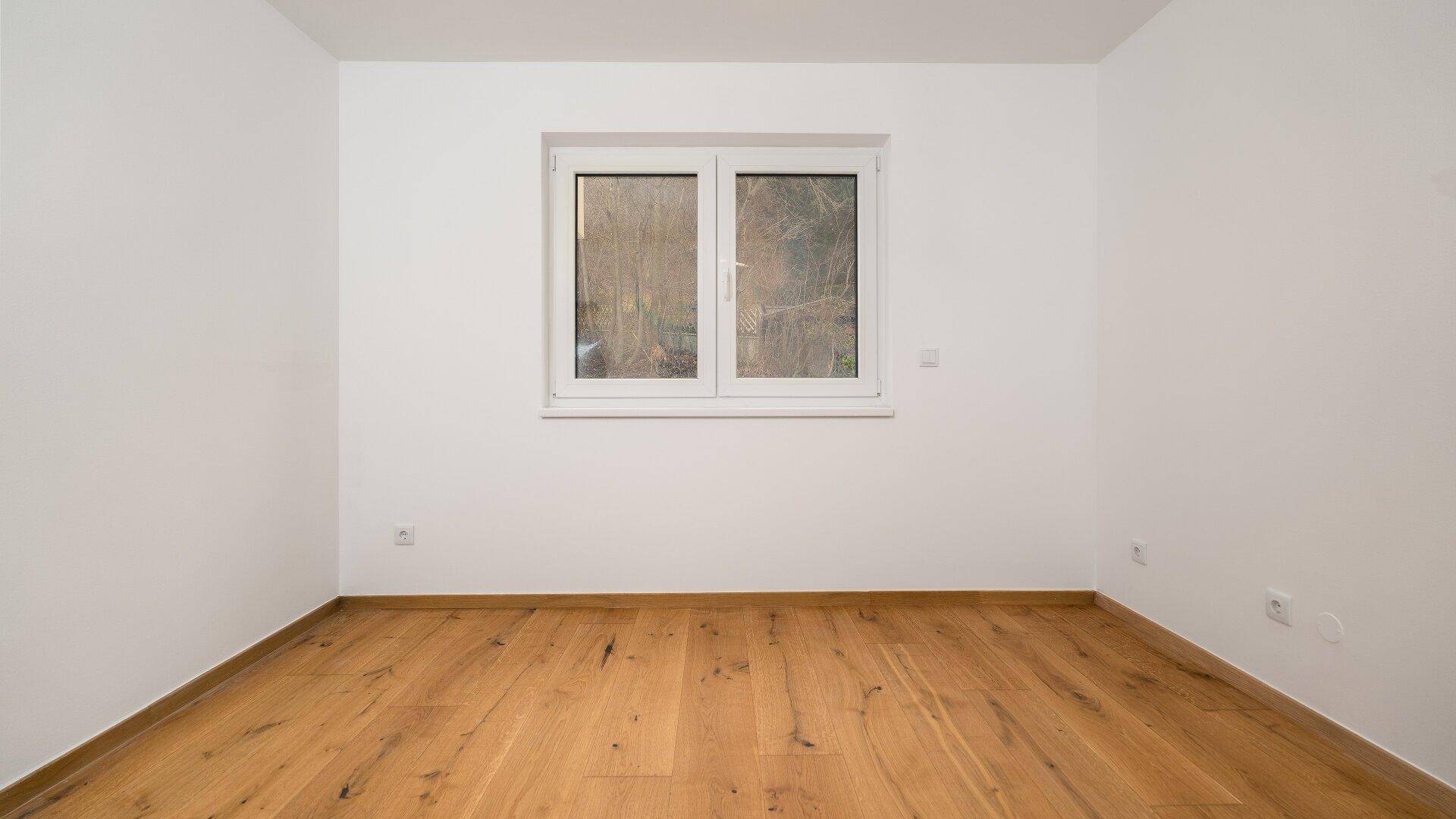 Helles Zimmer mit Holzboden und einem Fenster, ideal als Schlafzimmer oder Arbeitszimmer.