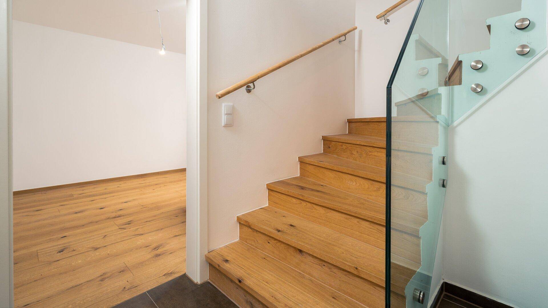 Moderne Holztreppe mit Glasgeländer, die zu den oberen Etagen führt, mit hellem Holzboden.