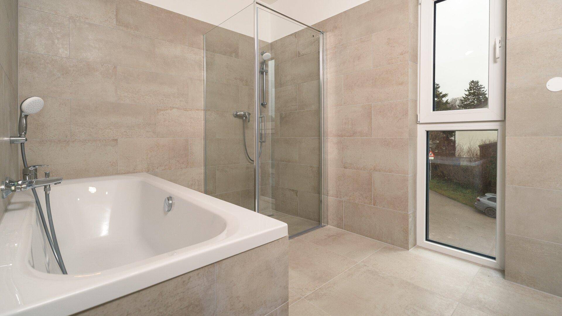 Modernes Badezimmer mit beigefarbenen Fliesen, Badewanne, begehbarer Dusche und Fenster.