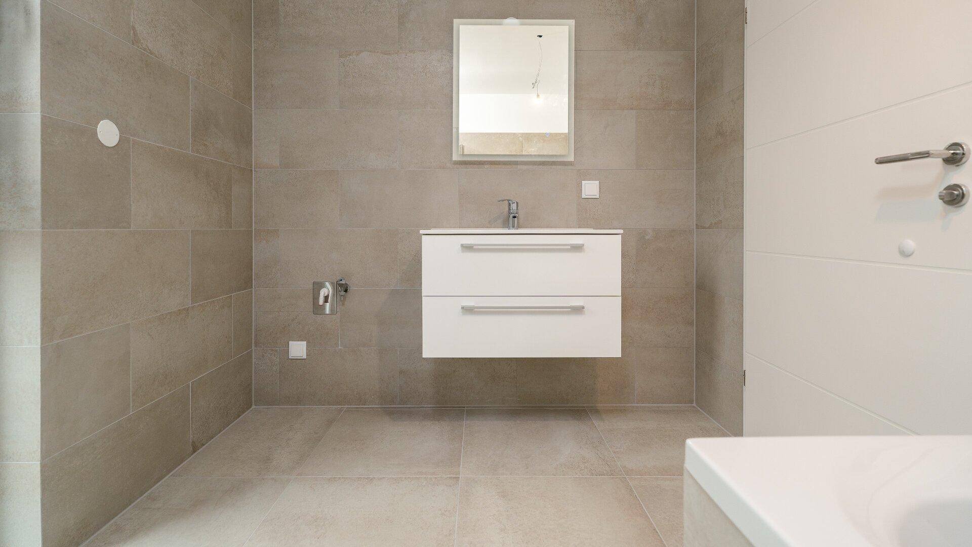 Helles Badezimmer mit beigefarbenen Fliesen, schwebendem Waschtisch mit Unterschrank und Spiegel.