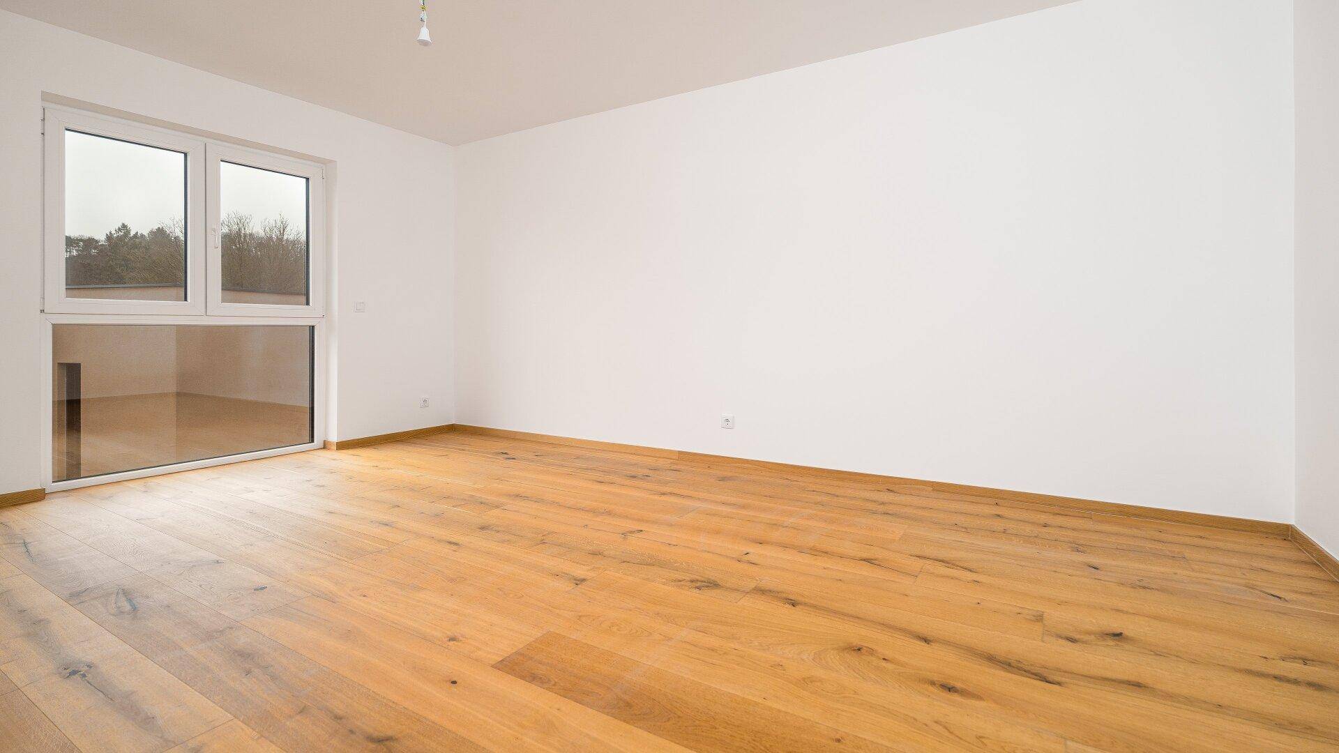 Helles Zimmer mit Holzboden und einer großen Fensterfront, die den Raum mit Licht füllt.