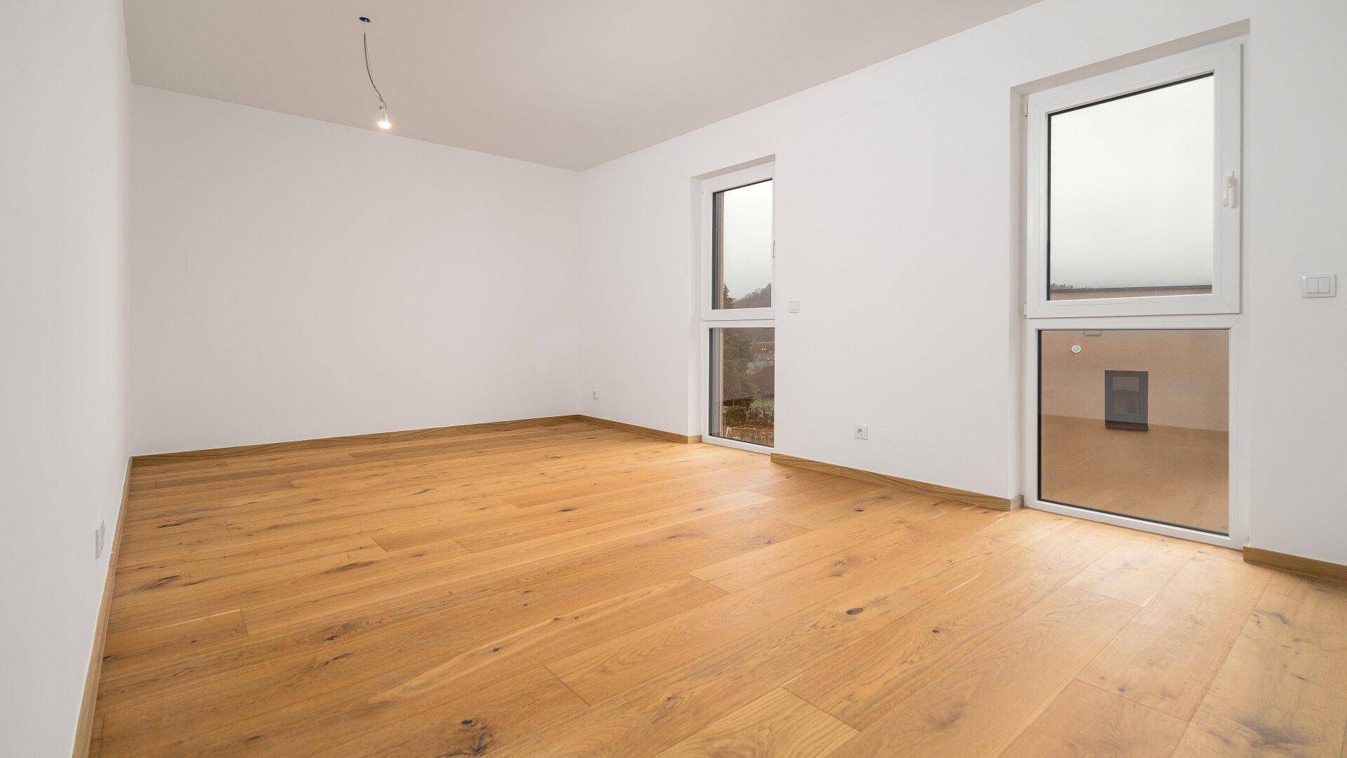 Geräumiges Zimmer mit Holzboden und zwei Fenstern, die für viel natürliches Licht sorgen.