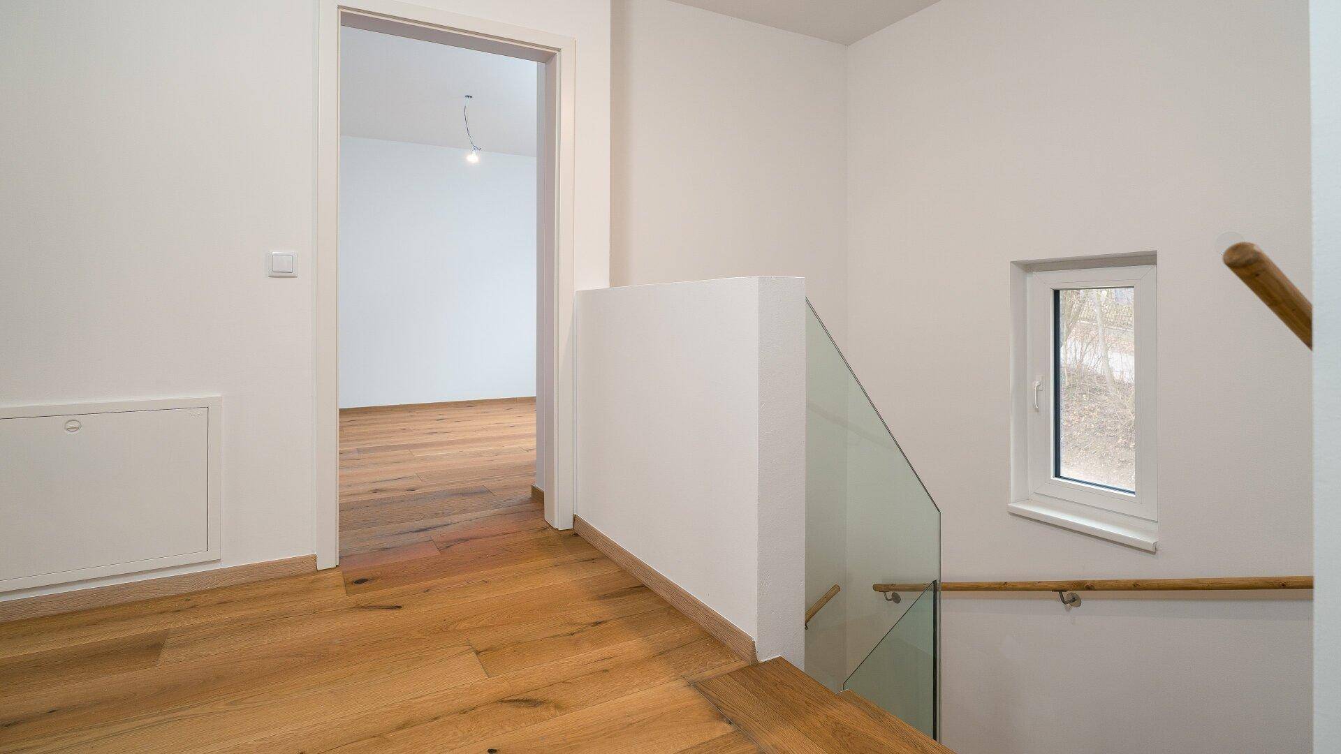 Heller Treppenabsatz mit Glasgeländer und Fenster, der zu weiteren Räumen führt.